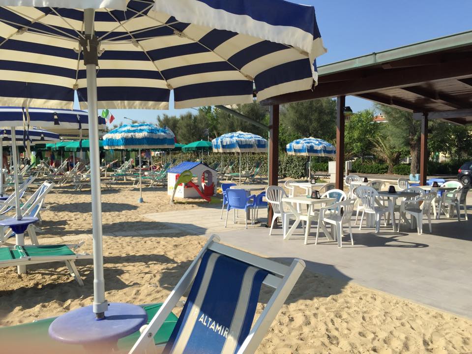 L'area bar e ristoro del lido con i tavoli sotto il gazebo, gli ombrelloni e la casetta giochi per bambini